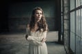 Beautiful girl in in white vintage dress with curly hair posing near the loft window. Woman in retro dress. Worried sensual emotio Royalty Free Stock Photo