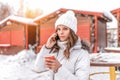 Beautiful girl in winter on street makes phone call, in her hand cup coffee tea, breakfast snack on nature. Warm jacket Royalty Free Stock Photo