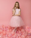 Beautiful girl 9-10 years old in pink clothes on a pink background among pink balloons. Stylish fashion photo for birthday cards,