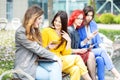 Beautiful girls are sitting with gadgets on the bench. Women communicate. The concept of the Internet, social networks, study and Royalty Free Stock Photo