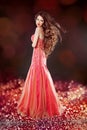 Beautiful glam with long hair posing in red dress over bokeh bright background.