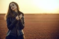 Beautiful glam model with long hair wearing black veiling dress and stylish leather jacket standing in the deserted field