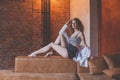 Beautiful glamorous stylish woman with curly hair sitting on the brown sofa against red brick studio wall background