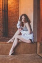 Beautiful glamorous stylish woman with curly hair sitting on the sofa on red brick studio wall