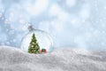 Beautiful glass ball with Christmas tree and gift on snow against light blue background, space for text. Bokeh effect Royalty Free Stock Photo