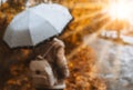 Beautiful golden autumn season. Watercolor like blurred blond girl with backpack and bright umbrella stands under rainy Royalty Free Stock Photo