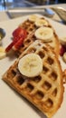 beautiful golden brown waffles covered in strawberries and banana slices with butter and syrup on a plate Royalty Free Stock Photo