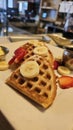 beautiful golden brown waffles covered in strawberries and banana slices with butter and syrup on a plate Royalty Free Stock Photo