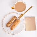 Golden colored eclairs on plate, knife and fork, cup of coffee