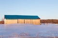 Beautiful golden hour winter view of patrimonial natural wood barn with steep blue metal roof in snowy field Royalty Free Stock Photo