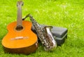 Beautiful golden saxophone and acoustic guitar lying across black instumental case on grassy surface Royalty Free Stock Photo