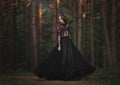 A beautiful gothic princess with pale skin and very long red hair in a black crown and a black long dress in a misty fairy forest. Royalty Free Stock Photo
