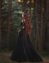 A beautiful gothic princess with pale skin and very long red hair in a black crown and a black long dress walks in a misty fairy-t