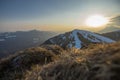 Beautiful grass patch on the top of Soriska Planina ski slope, viewed towards setting sun over majestic mountains in Slovenia
