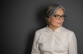 Beautiful gray-haired business woman looking at side. Mature woman in glasses and white shirt on grey background Royalty Free Stock Photo