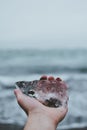 Beautiful gray Icelandic landscape behind a piece of crystal glacier held by a traveler in his hand