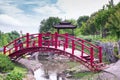 Beautiful green botanical landscape design in garden, city park with red wooden bridge through decorative lake pond