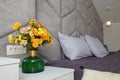 Beautiful grey bedroom, bed, pillows, soft fabric headboard, autumn bouquet of yellow chrysanthemums in green vase near. Modern Royalty Free Stock Photo