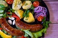 Beautiful grilled sausages on a black plate with vegetables and a background of boards