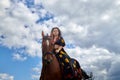 Beautiful gypsy girl on a horse in field with green glass in summer day and blue sky and white clouds background. Model in ethnic