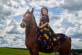 Beautiful gypsy girl on a horse in field with green glass in summer day and blue sky and white clouds background. Model in ethnic