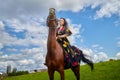 Beautiful gypsy girl on a horse in field with green glass in summer day and blue sky and white clouds background. Model in ethnic