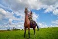 Beautiful gypsy girl on a horse in field with green glass in summer day and blue sky and white clouds background. Model in ethnic