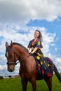 Beautiful gypsy girl on a horse in field with green glass in summer day and blue sky and white clouds background. Model in ethnic Royalty Free Stock Photo