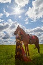 Beautiful gypsy girl with a horse in field with green glass in summer day and blue sky and white clouds background. Model in Royalty Free Stock Photo