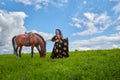 Beautiful gypsy girl with a horse in field with green glass in summer day and blue sky and white clouds background. Model in Royalty Free Stock Photo