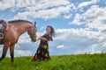 Beautiful gypsy girl leads a stubborn, unruly horse in field with green glass in summer day and blue sky and white clouds Royalty Free Stock Photo