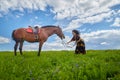 Beautiful gypsy girl leads a stubborn, unruly horse in field with green glass in summer day and blue sky and white clouds Royalty Free Stock Photo