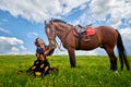 Beautiful gypsy girl sitting near horse in field with green glass in summer day and blue sky and white clouds background. Model in Royalty Free Stock Photo