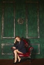 Beautiful half-naked brown-haired woman in the jacket sits in an armchair at darkgreen background