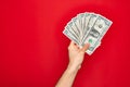 Beautiful hand of man holding bunch of dollar banknotes over isolated red background