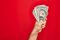 Beautiful hand of man holding bunch of dollar banknotes over isolated red background