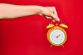 Beautiful hand of man holding vintage alarm clock over isolated red background Royalty Free Stock Photo