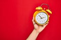 Beautiful hand of man holding vintage alarm clock over isolated red background Royalty Free Stock Photo