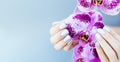 Beautiful hand with perfect nail pink manicure and purple orchid flower. on light blue background.