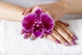 Beautiful hands with fresh lilac manicure lying on a white towel and over lilac purple orchid flower Royalty Free Stock Photo