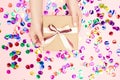 Beautiful hands girl hold gift box present craft paper on pink confetti background, flat lay. Concept Christmas, New Royalty Free Stock Photo
