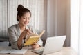 A happy Asian businesswoman is reading some details on her notebook while sitting at her desk Royalty Free Stock Photo