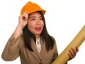 Beautiful and happy Asian Chinese woman in hardhat holding building blueprints as architect engineer or constructor supervisor in Royalty Free Stock Photo