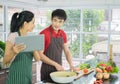 Beautiful happy asian couple are cooking in the kitchen. prepare salad food for diner. Man and Woman smiling looking menu from tab Royalty Free Stock Photo