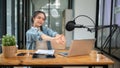 A happy Asian female radio host stretches her arms at her desk after finishing her live radio show Royalty Free Stock Photo