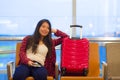 Beautiful and happy Asian Korean tourist woman with travel suitcase in airport sitting at departures waiting for flight smiling ch Royalty Free Stock Photo