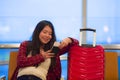 Beautiful and happy Asian Korean tourist woman with travel suitcase in airport sitting at departures waiting for flight smiling ch Royalty Free Stock Photo