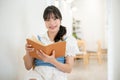 A beautiful and happy Asian woman enjoys reading a book while relaxing in a coffee shop Royalty Free Stock Photo