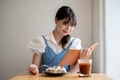 A beautiful and happy Asian woman is reading a book while relaxing in a cafe on the weekend Royalty Free Stock Photo