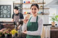 Beautiful happy asian young barista woman in apron holding cup coffee with serving to customer in cafe Royalty Free Stock Photo